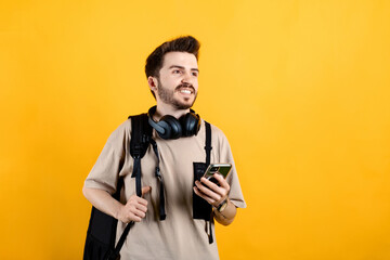 Young man wearing beige t-shirt posing isolated over yellow background looking far away to the front while holding a mobile phone.