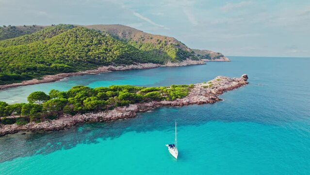 Vessel sailing by a Beautiful tropical green rocky coast with turquoise waters. Paradise alike bay in Cala Agulla, Mallorca, Balearic Islands, Spain with a tourist boat exploring the location.