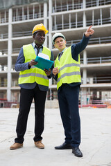 Young civil engineer discussing a construction plan with a colleague holding a folder of documents...