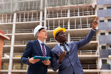 African-american architect discussing a construction plan with a colleague at a construction site points to something, ..pointing to it