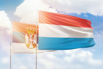 Sunny blue sky and flags of luxembourg and serbia
