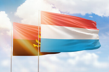 Sunny blue sky and flags of luxembourg and angola