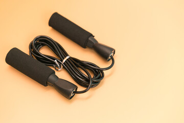 A black skipping rope lies down on the yellow background. Athletics. Effort. Gymnastic. Spirit. Endurance. Power. Weight. Leaping. Fit. Jumping. Sporting. Plastic. Object. Blue. Space. Element