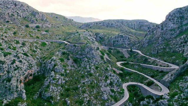 Cars, buses and motorcycles drive on European curved road in Majorca, Spain. Nus de Sa Corbata is a spectacular panoramic snake-like road with curves and rocky landscapes by the Mediterranean.