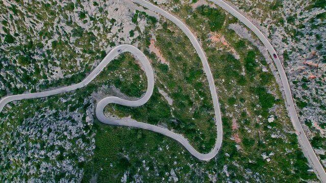 Cars, buses and motorcycles drive on European curved road in Majorca, Spain. Nus de Sa Corbata is a spectacular panoramic snake-like road with curves and rocky landscapes by the Mediterranean.
