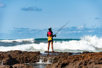 Fisherman woman with fishing rod on the rocks fishing