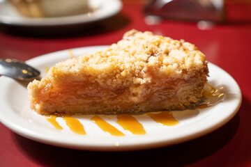 a portion of apple pie with sauce on a red table