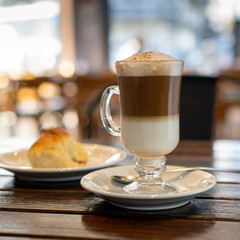 a cup of cappuccino with a croissant on a table in a bar.