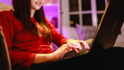 Focus hand of woman working overtime by laptop on armchair at home at night