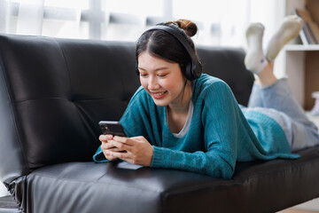 Asian Smiling girl relaxing at home, she is playing music using a smartphone and wearing white headphones