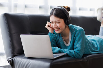 Asian young female student sitting at the table, using laptop and headphones when studying.