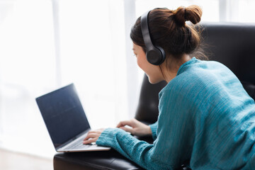Asian young female student sitting at the table, using laptop and headphones when studying.
