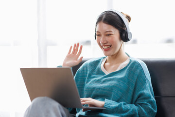 Asian young female student sitting at the table, using laptop and headphones when studying.