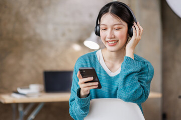 Smiling girl relaxing at home, she is playing music using a smartphone and wearing white headphones