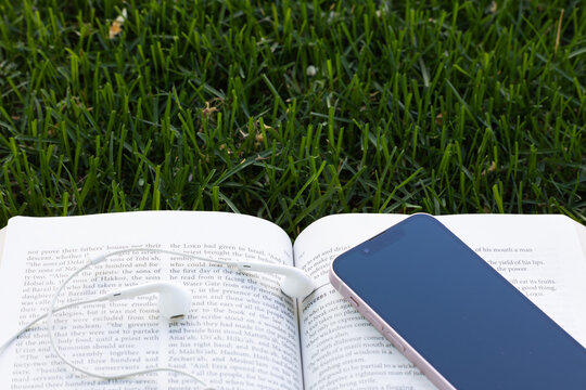Open bible with mobile phone and headphones laying on the grass with copy space