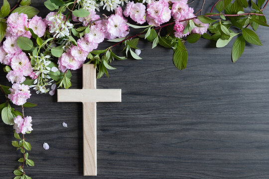 Wood cross with border of branches with pink and white flower blossoms on a dark wood background with copy space