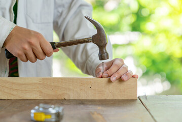 Close up hammering a nail into wooden bar on the table.