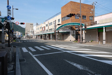 人通りの少ない時間帯の交差点と信号機、道路の両側に商店がある大通り（日本の地方都市） - obrazy, fototapety, plakaty