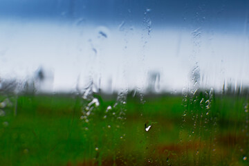 Abstract image of monsoon, blurred blue sky with green natural foreground and raindrops on glass creating rainy mood. Rainy season or monsoon season of rural India.