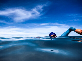 Open Water female swimmer doing freestyle  in glassy ocean wearing goggles, wetsuit and cap