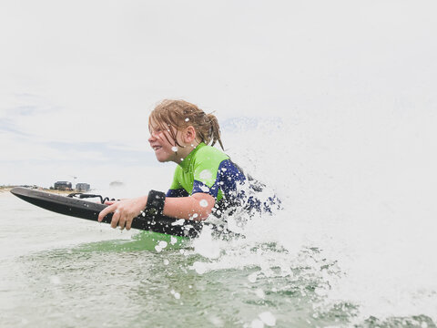Young boy in wetsuit riding boogie board in waves at beach