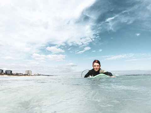 Young boy paddling surfboard in ocean looking at camera with high rise buildings in background