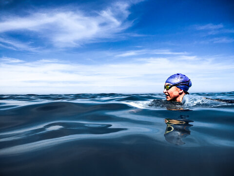Swimmer wearing goggles and cap in open blue ocean water doing breaststroke looking ahead