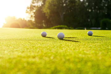 Three golf balls on the green grass near hole on a golf course at sunset