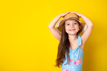 Summer vacation by the sea. Portrait of a cheerful girl in a blue swimsuit and hat on a colored yellow background. Space for text