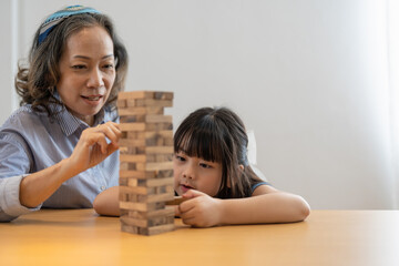 Obraz na płótnie Canvas Happy moments of Asian grandmother with her granddaughter playing jenga constructor. Leisure activities for children at home.
