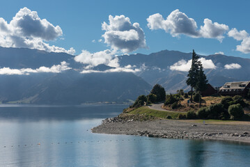 Headland overlooking Lake Hawea in morning light with small, puffy clouds and mountains in the...