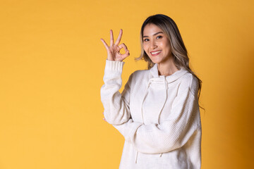 A young Asia woman with long hair in a knitted sweater color white facial expression and use sign language for communication on  yellow background.