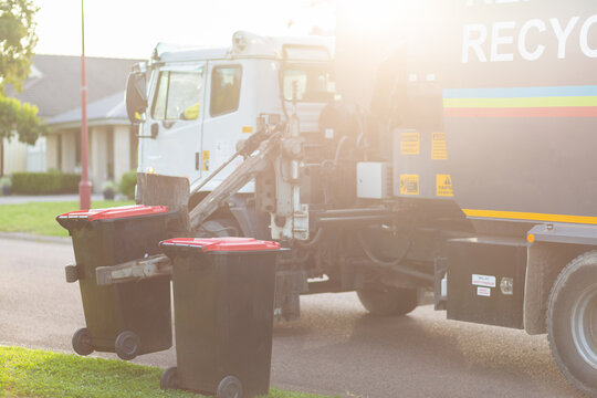 Garbage truck picking up bins from curb side in suburban area