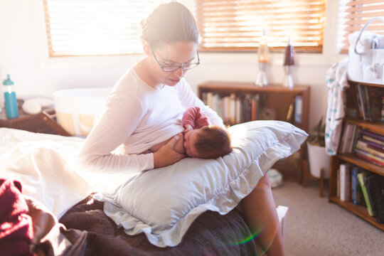 Young mum in bedroom breastfeeding content newborn baby with light flare