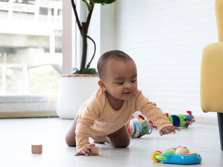 Cute little African baby crawling around the room to get colorful toys.
