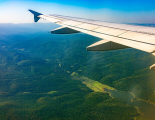 View of airplane wing, blue skies and green land during landing. Airplane window view.