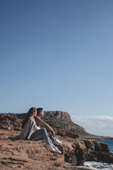 Young couple is sitting in front of Cape Greco mountain and looking at seashore