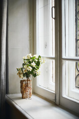 A bouquet of jasmine flowers in a wine glass on a windowsill. Vertical photo.