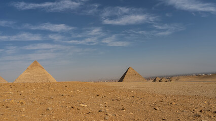 Fototapeta na wymiar The great pyramids of Chephren, Mykerinus and the small pyramids of queens against the blue sky. Stones on the yellow sand of the Giza plateau. The houses of Cairo are visible in the distance. Egypt