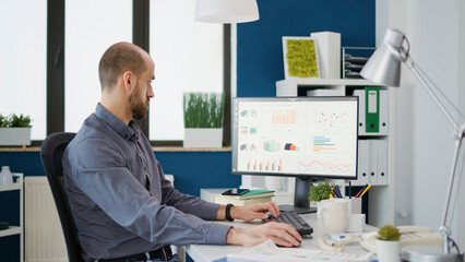 Business man doing financial research on computer in startup office to work on sales development. Executive assistant using marketing statistics to plan charts and graphs presentation.