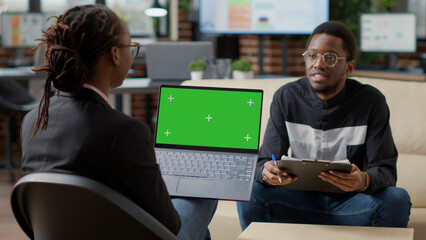 Female employee with greenscreen on laptop interviewing man, talking about business strategy. Woman using isolated chroma key with mockup template and blank copyspace on computer. Tripod shot.