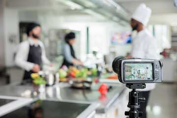 Selective focus of camera filming restaurant kitchen chefs preparing gourmet dish for culinary...