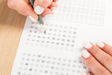 Students hands to take exams, writing an exam room with a pencil holding on an optical form of a standardized test with answers 
