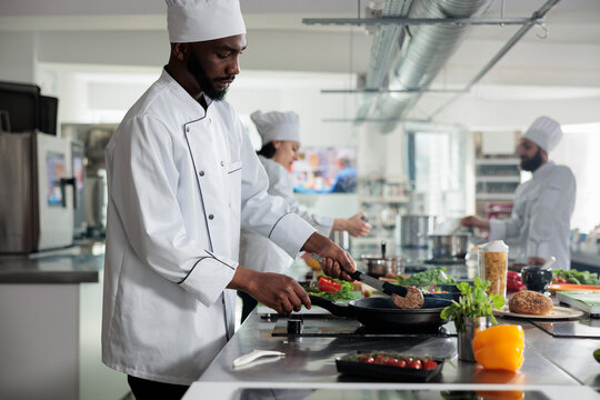 Sous chef cooking delicious gourmet dish while preparing meat in pan inside kitchen. African american head cook searing succulent beef patty while preparing food for dinner service at restaurant.