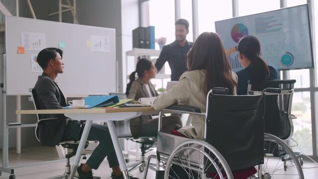 A disabled company employee is able to work happily with colleagues in the office. A group of marketers are having a discussion at the meeting.