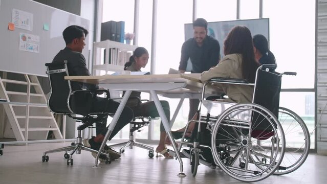 A disabled company employee is able to work happily with colleagues in the office. A group of marketers are having a discussion at the meeting.