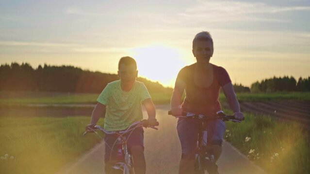 Mom and son on a sunset walk on bicycles. Family woman and teenager child ride on the path in the park on bicycles.