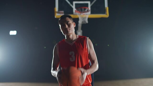 Slow motion, portrait of an asian man basketball player, throws the ball in his hands, serious looking at the camera, basketball championship.