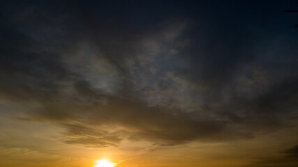 Dramatic sunset landscape with puffy clouds lit by orange setting sun and blue sky