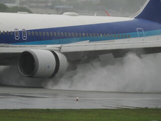 雨の日の滑走路に着陸した旅客機の逆噴射で巻き上がった水煙